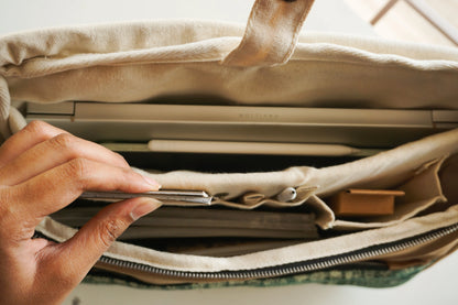 Eco-friendly canvas laptop bag with tan handle and plant, sustainable and affordable